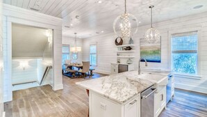 A spacious kitchen with a marble countertop, pendant lighting, and a view of the outdoors through large windows. - h2o365-The Heart of Seagrove (Santa Rosa Beach)