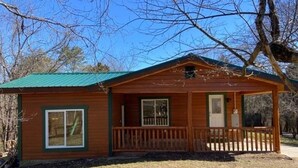 A small wooden cabin with a green roof, a front porch, and a fenced yard. - Property has a small pond on back side of the cabin ,it has geese  and ducks . (Sevierville)