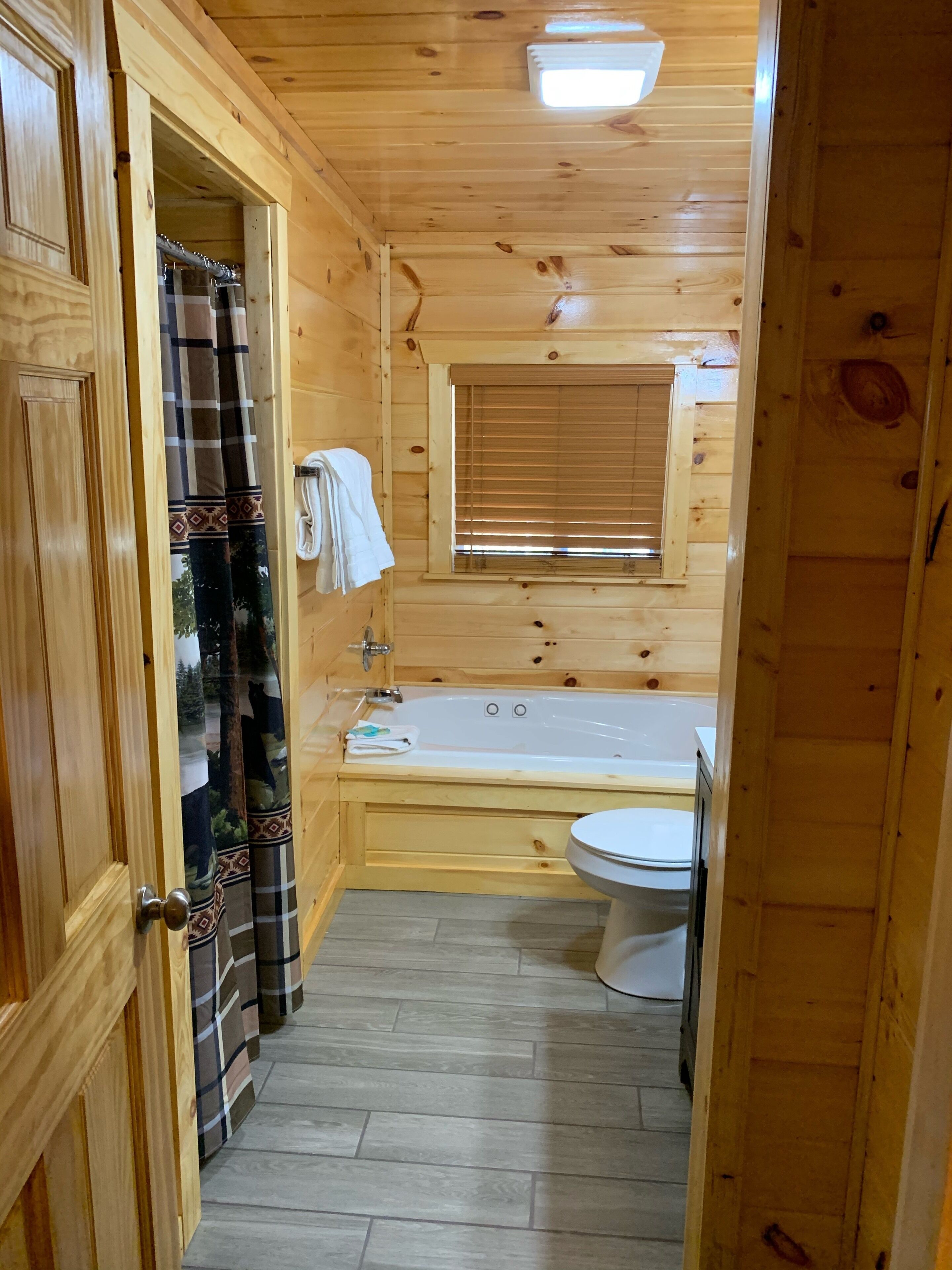 Baño de cabaña de madera con bañera, inodoro y ventana con persianas.