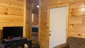 A wooden cabin interior with a ceiling fan, a television on a desk, a floral sofa, and a door. - Property has a small pond on back side of the cabin ,it has geese  and ducks . (Sevierville)