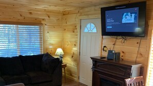 A cozy cabin interior with a wooden floor, a sofa, a television mounted on the wall, and a fireplace. - Property has a small pond on back side of the cabin ,it has geese  and ducks . (Sevierville)
