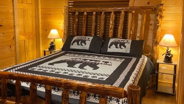 A wooden cabin-style bedroom with a bed featuring a bear-themed bedspread, two bedside lamps, and a wooden headboard. - Property has a small pond on back side of the cabin ,it has geese  and ducks . (Sevierville)