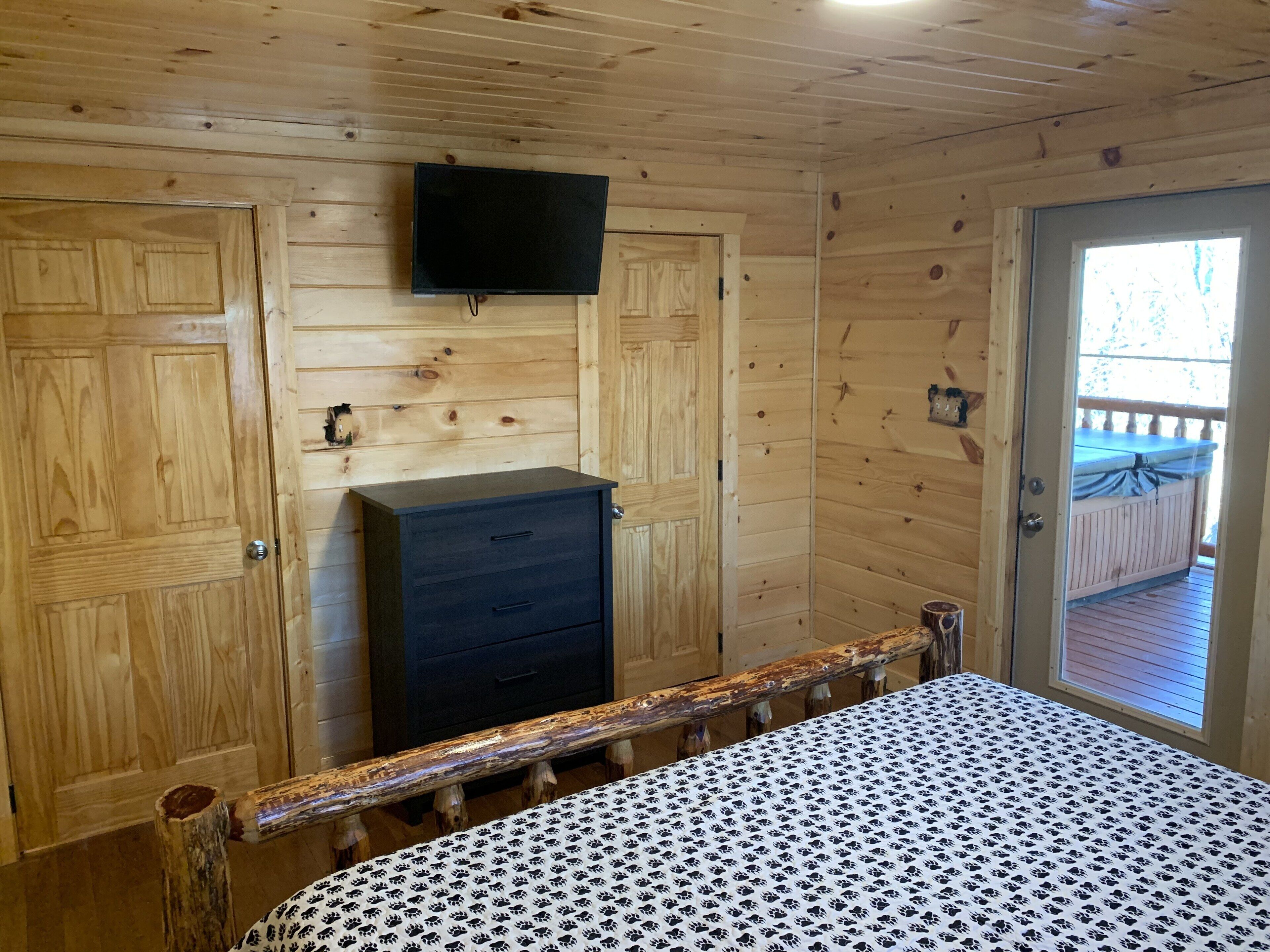 Una habitación tipo cabaña de madera con una cama, cómoda y televisor fijado en la pared.