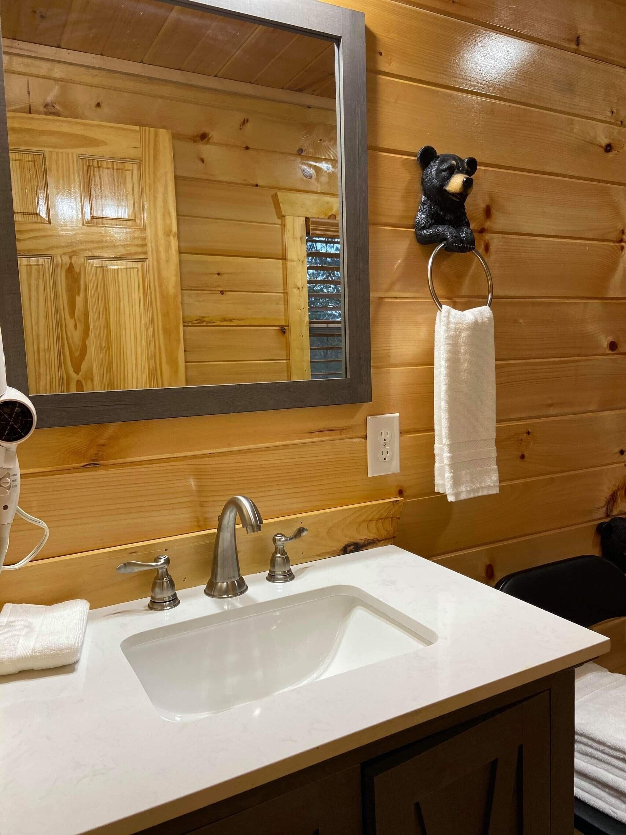 A bathroom with a wooden wall, a large mirror, a sink with a faucet, and a towel ring with a white towel.