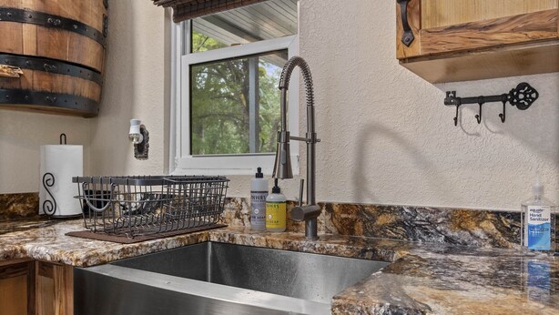 A kitchen with a stainless steel sink, a dish rack, a window, and wooden cabinets. - Weeki Wachee Pirate House (Spring Hill)
