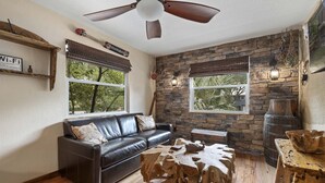 A cozy living room with a stone wall, a black leather sofa, wooden coffee table, and a ceiling fan. - Weeki Wachee Pirate House (Spring Hill)