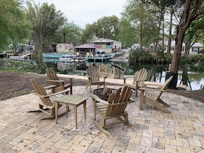 A lakeside patio with Adirondack chairs, a fire pit, and a view of boats and houses across the water. - Weeki Wachee Pirate House (Spring Hill)