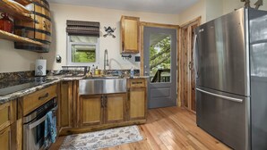 A kitchen with wooden cabinets, a stainless steel refrigerator, and a window overlooking greenery. - Weeki Wachee Pirate House (Spring Hill)