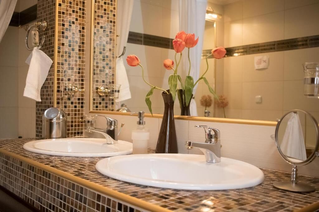 A bathroom with two sinks, a mirror, and a vase with flowers.