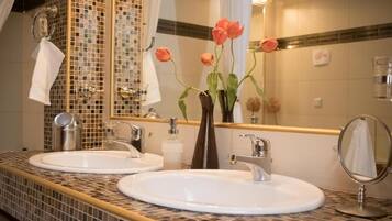 A bathroom with two sinks, a mirror, and a vase with flowers.