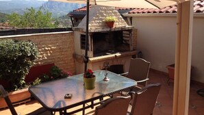 Une terrasse extérieure avec un barbecue, une table, des chaises et une vue sur les montagnes.
