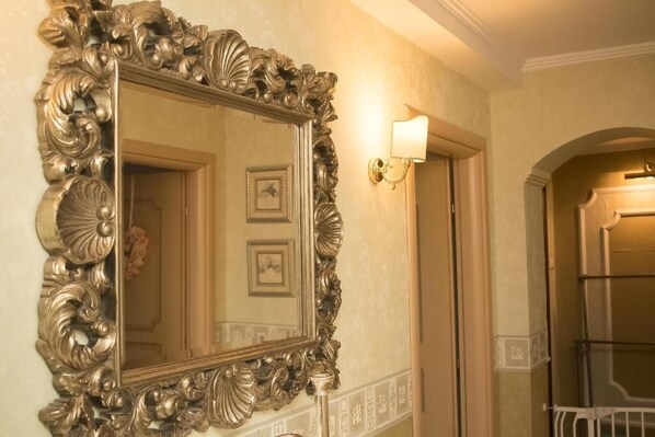 A bathroom with a large ornate mirror, a wall-mounted light fixture, and a framed picture on the wall.