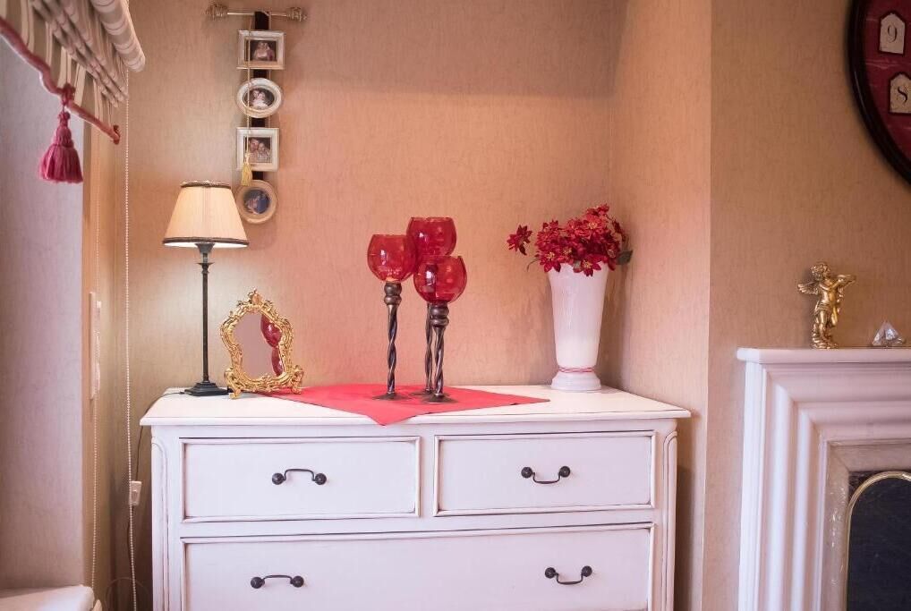 Une commode blanche à trois tiroirs, un tissu rouge et un vase avec des fleurs rouges.