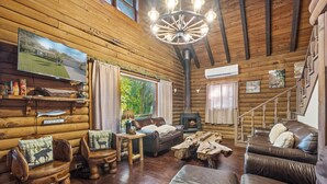 L’intérieur d’un chalet confortable, avec des murs en bois, une cheminée, des meubles en cuir et un téléviseur fixé au mur.
