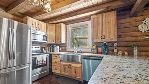 Une cuisine moderne avec des meubles en bois, des appareils en acier inoxydable, des plans de travail en granit et une fenêtre équipée de stores.