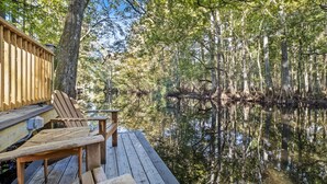 Une terrasse en bois, avec des chaises et une table, donnant sur une zone marécageuse bordée d’arbres et d’eau.