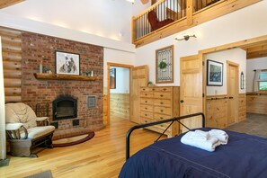 A cozy room with a fireplace, wooden furniture, and a bed with towels. - Rock Garden Roost | Stunning Mountain Views, Hot Tub, Game Room & Fire Pit! (Black Mountain)