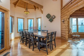 A spacious dining area with a wooden table and chairs, large windows, and a wooden ceiling. - Rock Garden Roost | Stunning Mountain Views, Hot Tub, Game Room & Fire Pit! (Black Mountain)