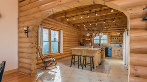 Interno di una baita con angolo cottura, pavimento in legno e una poltrona a dondolo.
