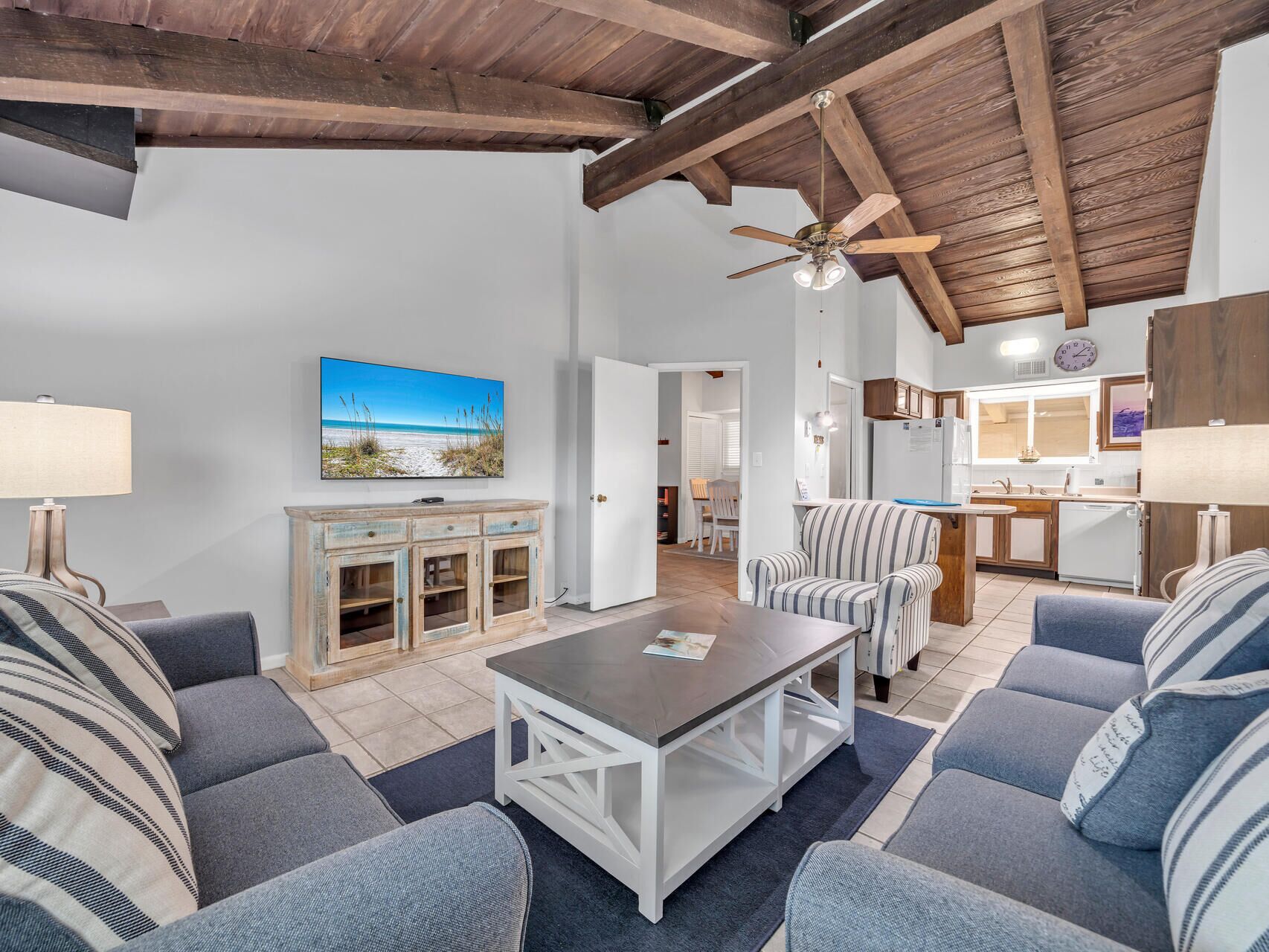 A living room with a ceiling fan, a TV, and a dining area with a kitchen in the background.