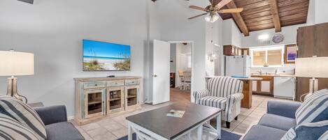 A living room with a ceiling fan, a TV, and a dining area with a kitchen in the background.