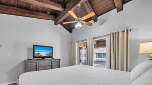 Habitación de hotel con una cama grande, televisor en una cómoda, ventilador de techo y balcón con cortinas.