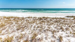 Una playa de arena blanca y vegetación escasa que desemboca en el océano.