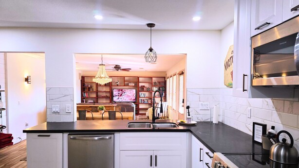 A modern kitchen with a dishwasher, stove, and a dining area with a TV. - Peaceful 55+ Retreat, Fully Stocked, Ideal for Long Stays, Updated Home (Sun City)