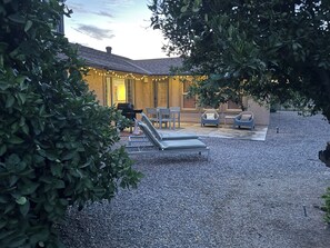 A patio area with lounge chairs, a barbecue grill, and string lights.