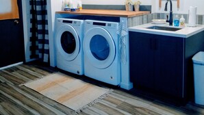 A laundry room with two front-loading washing machines, a sink, and a sign that reads "LAUNDRY CO." - Peaceful 55+ Retreat, Fully Stocked, Ideal for Long Stays, Updated Home (Sun City)