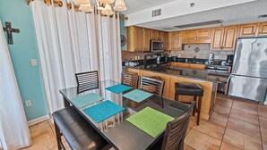 Una cocina moderna con armarios de madera, un refrigerador de acero inoxidable y una zona de comedor con mesa y sillas de vidrio.