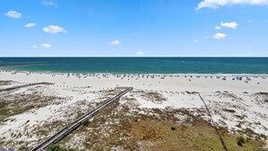 Una playa con un paseo marítimo de madera que conduce a la orilla, arena y cielo azul despejado.