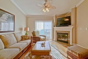 Una sala de estar con sofá, sillón, mesa de centro, chimenea, televisor y ventilador de techo.