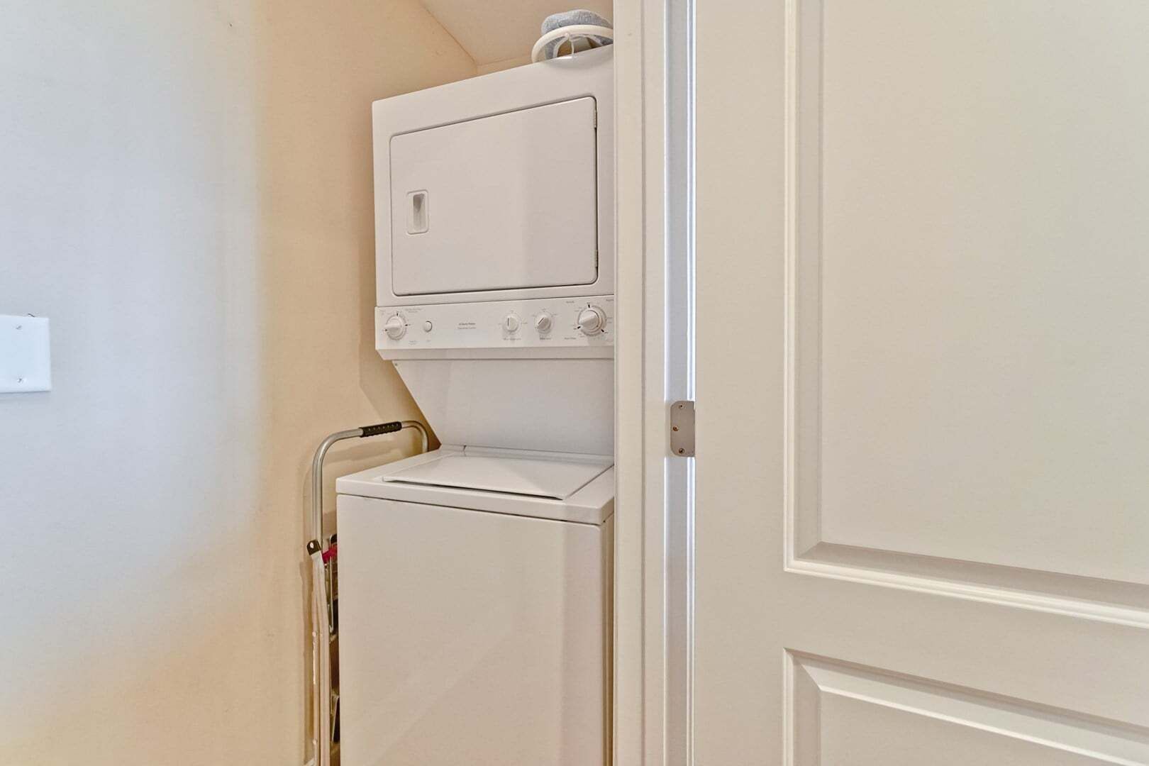 A compact laundry room with a stacked washer and dryer, a metal laundry cart, and a door.
