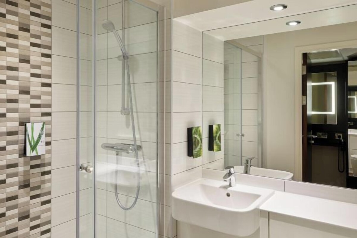 A modern bathroom with a glass shower enclosure, a white sink, and a large mirror.