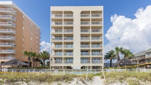 Ein Hotel direkt am Strand mit mehreren Balkonen, einem Sandstrand davor und Palmen.