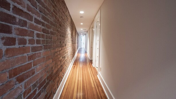 Ein schmaler Flur mit einer Backsteinwand und Holzdielen.