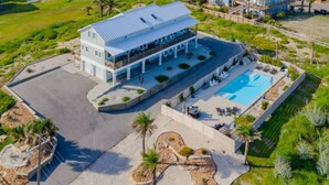A large two-story building with a swimming pool, surrounded by landscaped areas and palm trees. - Sandcastle Beach House, Ocean Views, 5Bed 4.5Bath, Huge Outdoor Private Pool (Port Aransas,)