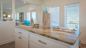 A kitchen with a marble countertop, white cabinetry, and a large mirror above the sink. - Sandcastle Beach House, Ocean Views, 5Bed 4.5Bath, Huge Outdoor Private Pool (Port Aransas,)