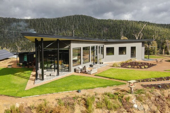 A modern house with a covered patio, large windows, and a well-maintained lawn. - The Retreat B&B, offgrid luxury (Buxton)