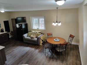A compact kitchen with a dining area, a black refrigerator, a gray sofa, and a wooden dining table with chairs. - Three-story Canadian Lighthouse (Fryeburg)