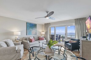 A spacious living room with a balcony, a ceiling fan, and a large painting.