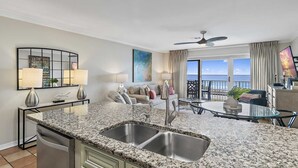 Una cocina moderna con encimeras de granito, un lavamanos doble y una zona de comedor con mesa de vidrio.