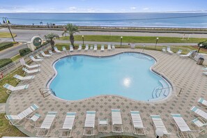 Una piscina con borde ondulado, rodeada de sillas de descanso y un patio con baldosas.