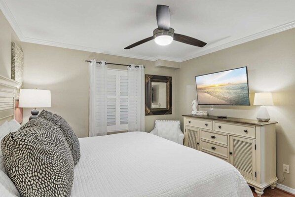A bedroom with a bed, a dresser, a television, and a ceiling fan.