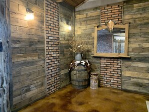 Un intérieur rustique avec des murs en bois, un mur d’accent en briques, un tonneau en bois, une peau de vache et un vase contenant des plantes séchées.
