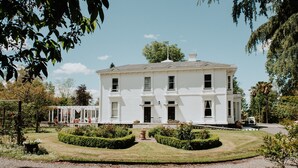 A large white building with a symmetrical facade, a covered porch, and a well-maintained garden with hedges and a central pathway. - Mt Vernon Villa (Waipukurau)