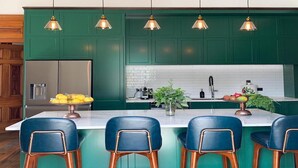 A modern kitchen with green cabinets, a stainless steel refrigerator, a marble island with bar stools, and pendant lighting. - Mt Vernon Villa (Waipukurau)