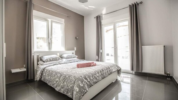Un dormitorio moderno con una cama grande, una mesita de noche, un radiador y vistas al exterior a través de la ventana.