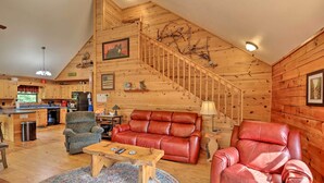 A spacious living area with a wooden staircase, leather sofas, and a wooden coffee table. - 'River's Edge' - Ultimate Riverfront Getaway (Hayesville)